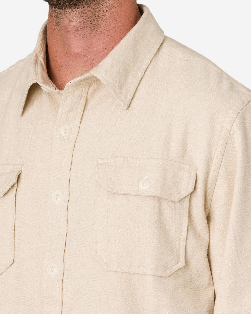 Close-up of a man wearing an Ace Rivington Flannel Ecru color utility button-up H3 shirt with two chest pockets, each with a flap secured by a button. The shirt has a collar and buttoned cuffs. The focus is on the upper torso, showcasing the shirt's design and details.