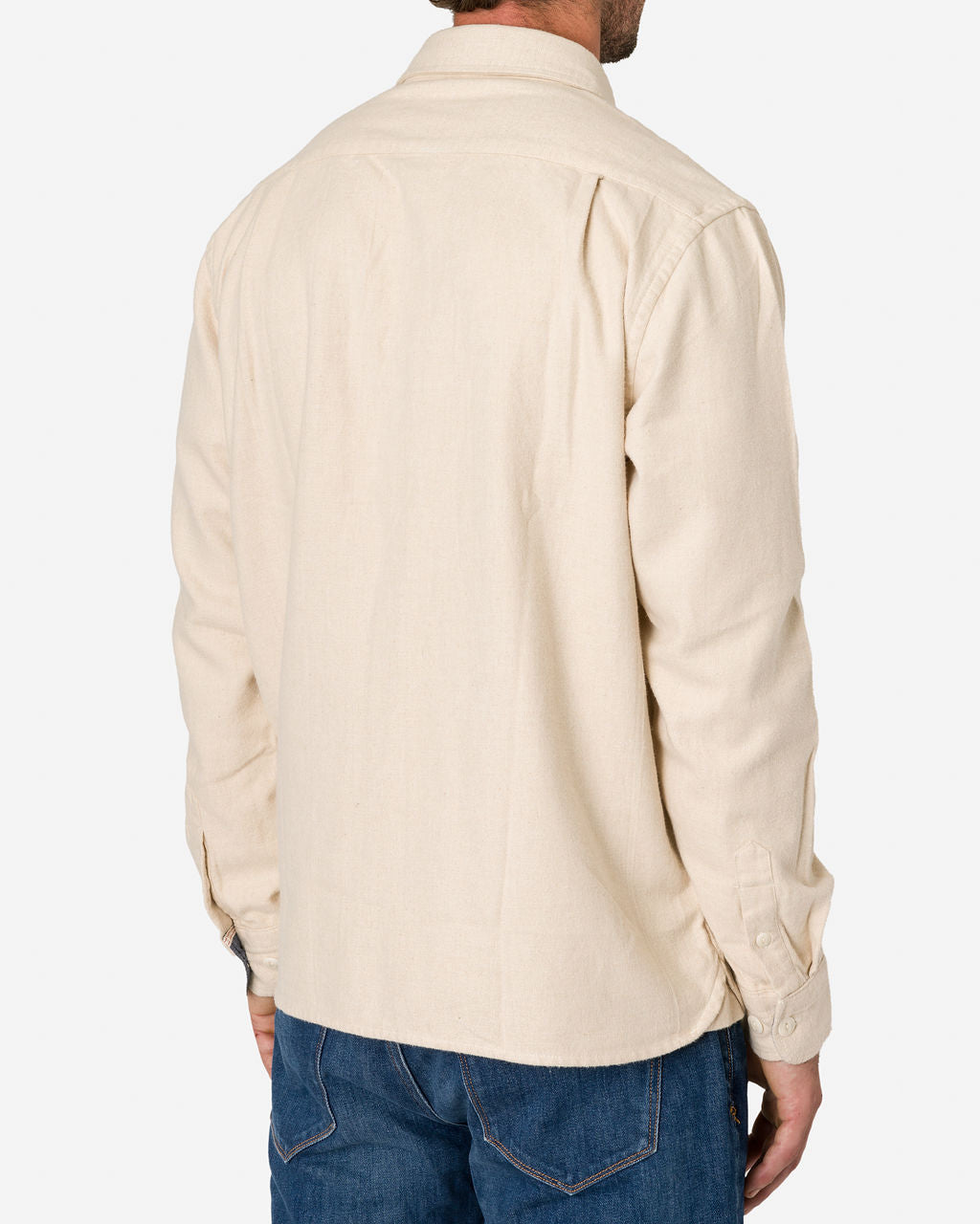 Man is shown from the back wearing an Ecru Flannel - Utility Shirt long-sleeve with buttoned cuffs and blue jeans by Ace Rivington. The shirt has a collar and a slightly curved hem and features visible stitching on the back pockets. The background is plain white, highlighting the clothing's fit and style.