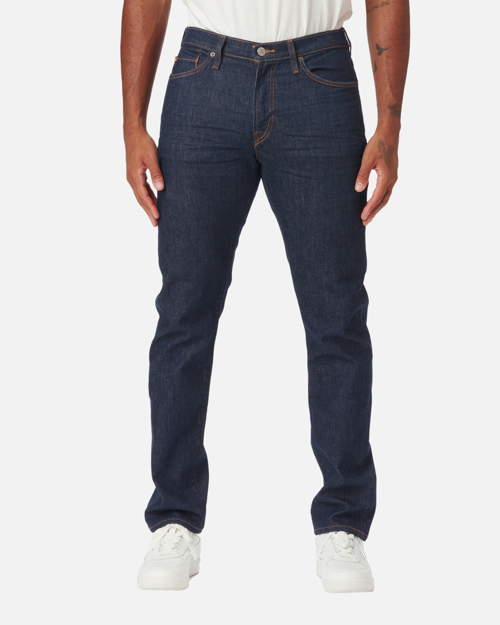 Model facing directly frontward wearing dark blue indigo men's Ace Rivington athletic taper jeans with no wear with a pair of white Diadora B Elite sneaker shoes and tucked white Ace Rivington super soft supima short-sleeved tee shirt