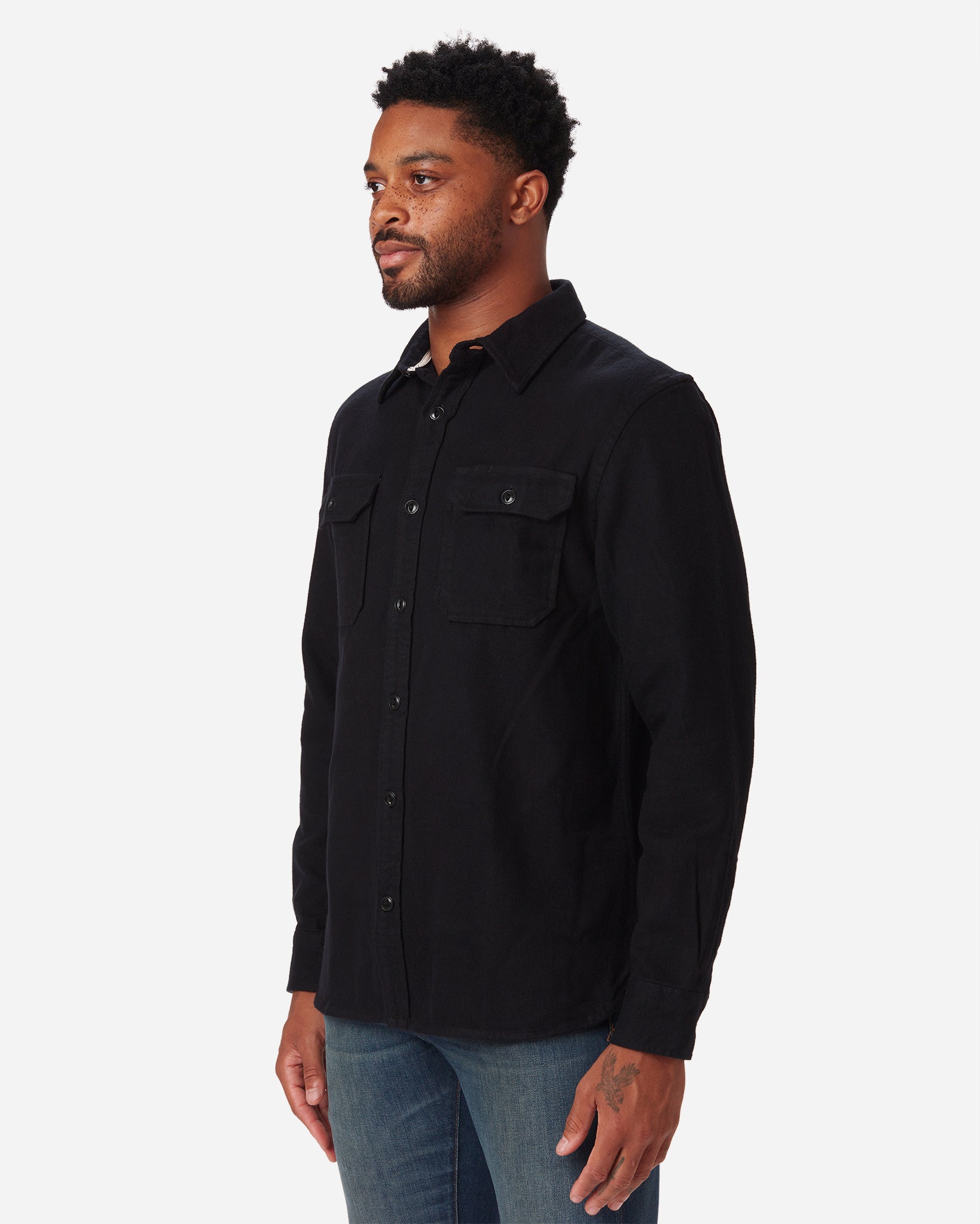 front of model wearing Ace Rivington men's black soft brushed flannel shirt with color matched buttons and breast pockets and dirty vintage blue denim jeans with slight stylistic thigh wear with a rightward gaze