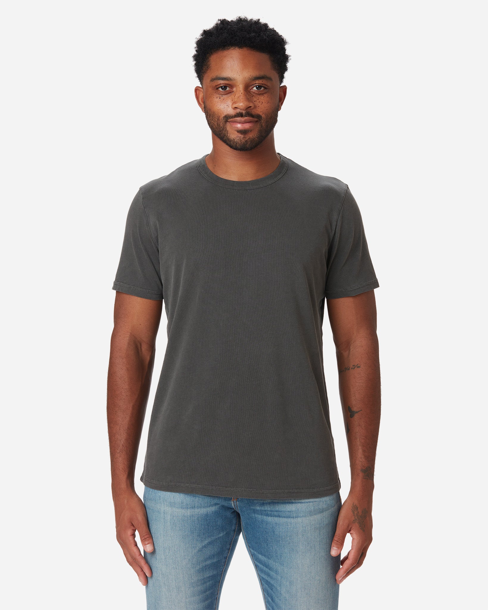 model facing directly forward wearing Ace Rivington long staple grey carbon colored super soft short-sleeved cotton shirt and a pair of Ace Rivington medium vintage medium light blue denim jeans