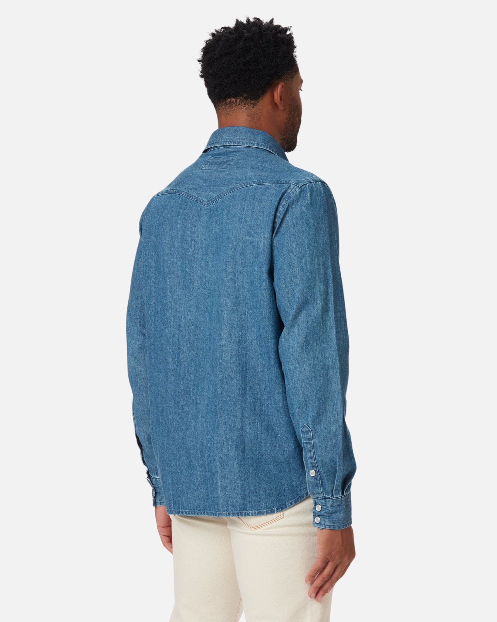 Man is shown in the image of the back wearing an Ace Rivington Mid Weight Denim Western Shirt in a medium wash paired with light-colored pants highlighting the fit and style of the shirt, showcasing its casual yet stylish design. The shirt has a classic denim look with a yoke design on the back and buttoned cuffs.