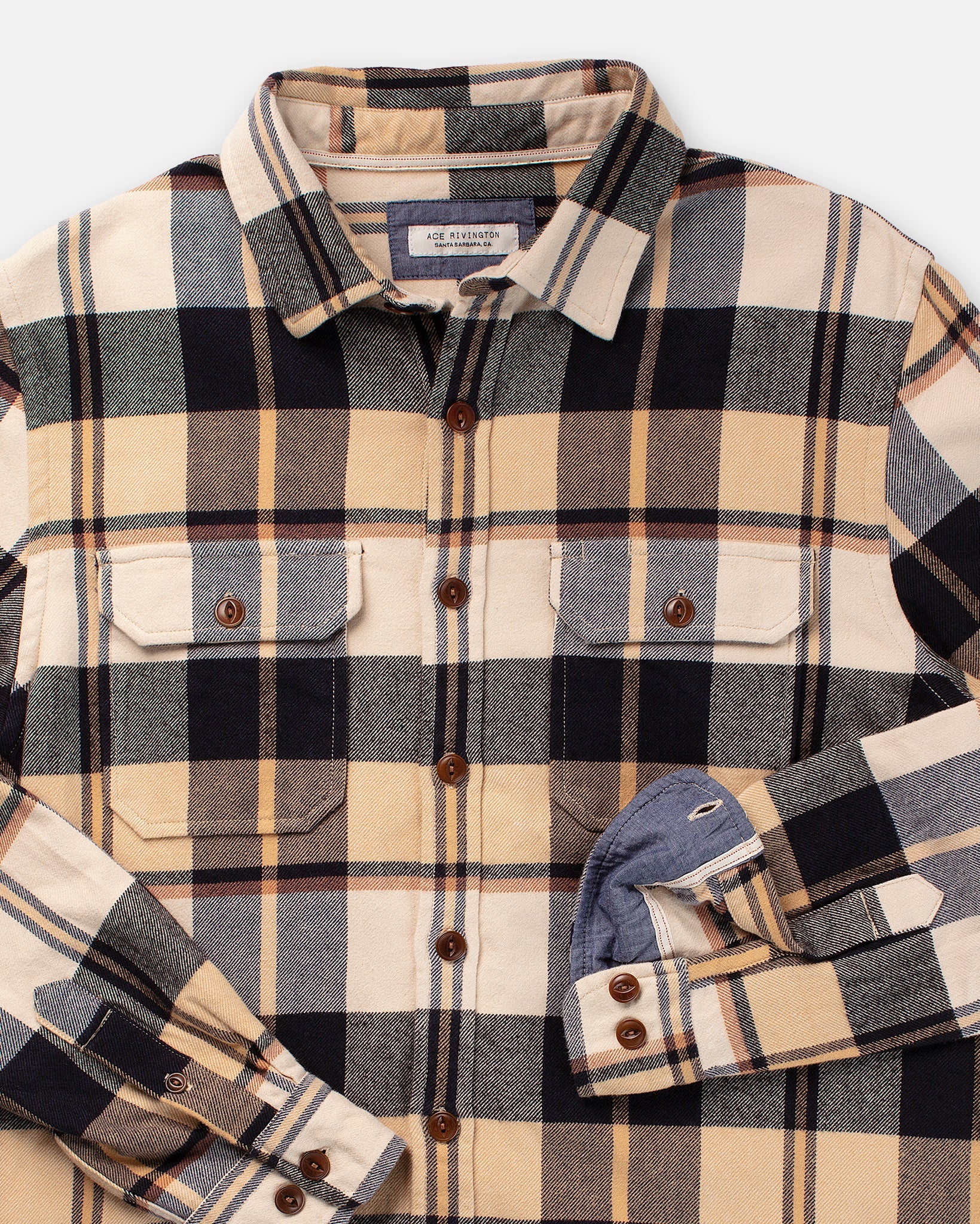 Flannel Utility Shirt - Midnight Dune with a pattern of beige, black, gray, and yellow checkered pattern. The shirt features a button-down front with brown buttons, two chest pockets with buttoned flaps, and a folded sleeve showing the inner lining. The shirt has a classic collar and is laid flat against a white background.