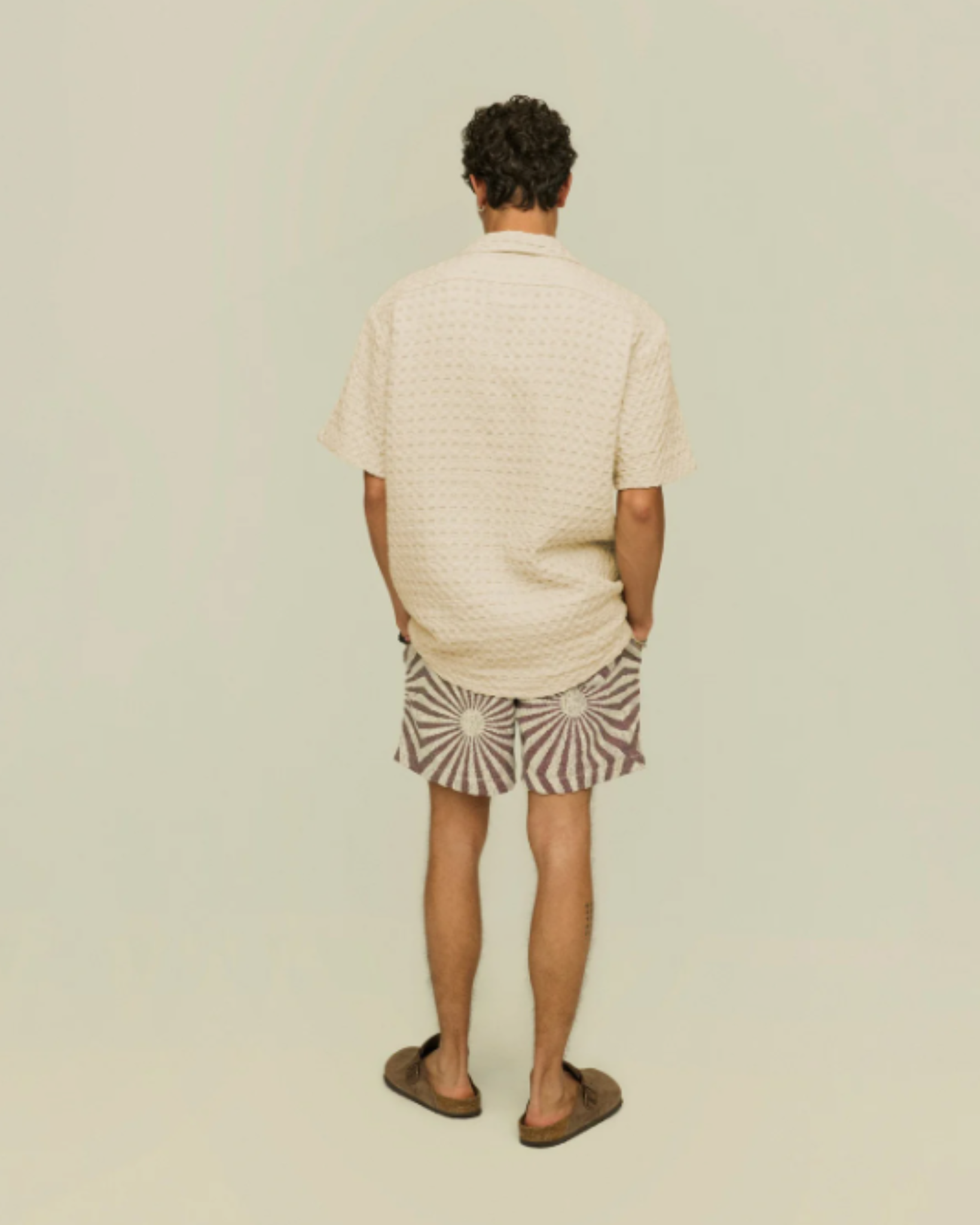 OAS Waffle - Cuba Shirt - Ecru shown from the back on a model, illustrating the shirt’s casual fit and drape paired with graphic shorts and brown shoes.
