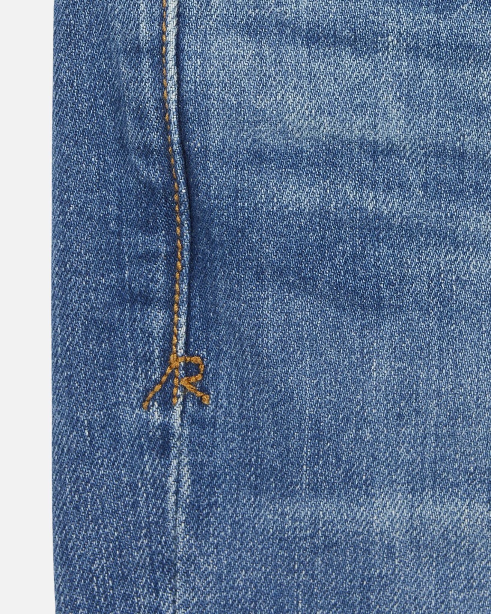 close up of stitching on pair of high quality slim cut men's light blue jeans with slight wear