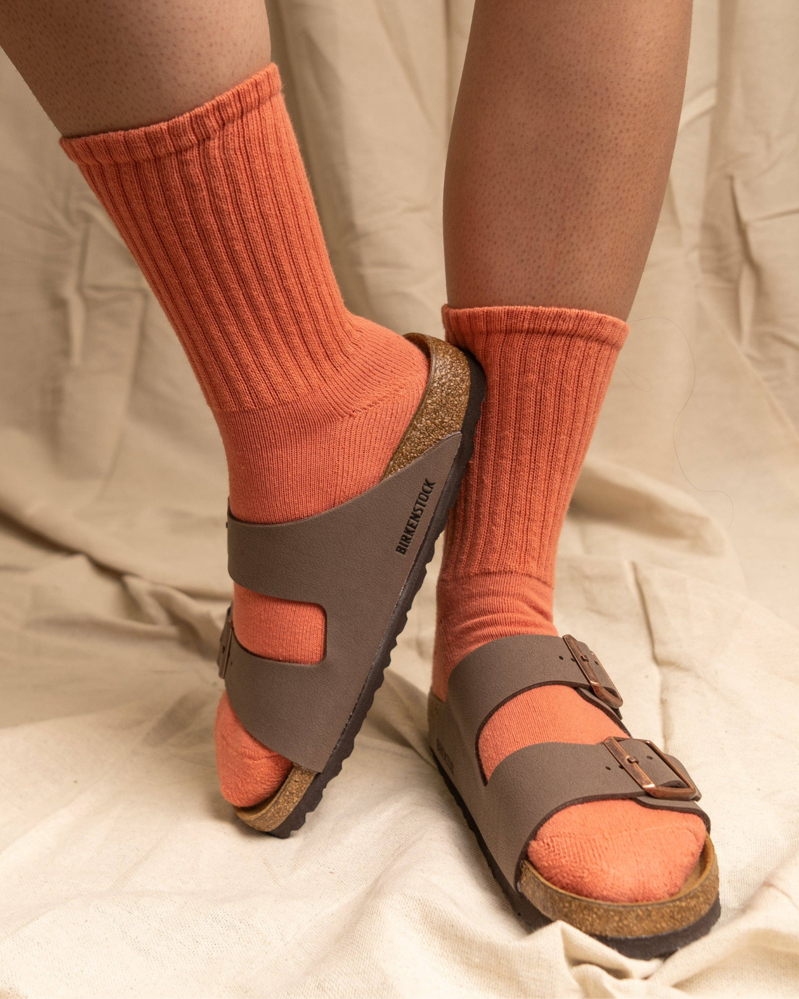 The Solids - Pumpkin worn with brown Birkenstock sandals in a lifestyle setting with a neutral fabric backdrop.