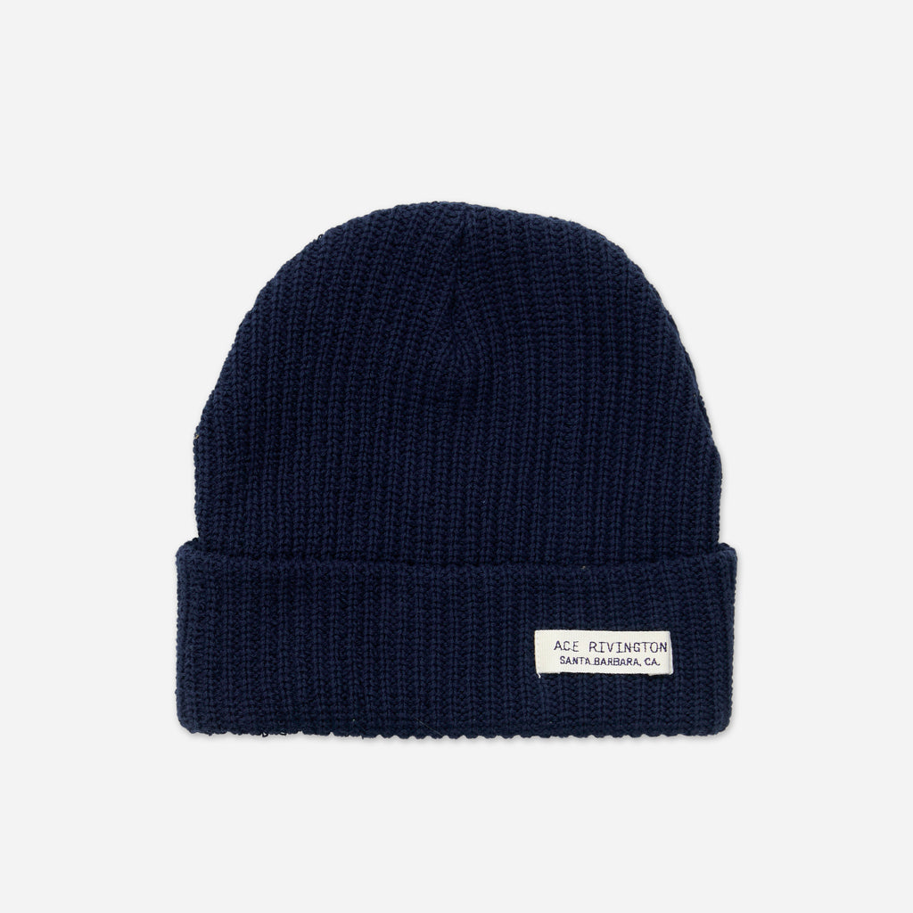 A navy blue-colored, Organic Cotton Beanie features a ribbed knit texture and a folded brim with a small white label that reads 'ACE RIVINGTON SANTA BARBARA, CA.'