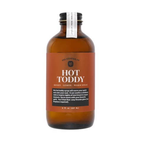 A brown glass bottle labeled 'Hot Toddy Syrup' from The Cocktail Co. The label highlights ingredients including honey, lemon, and warm spices. The bottle is 8 fl oz (237 ml) and suggests mixing the syrup with hot water and a spirit for a cozy, warming drink.