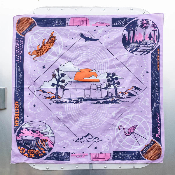 The Ace Rivington Bandits Bandana - Purple Venture With Curiosity features a purple background with illustrations of an Airstream trailer, mountains, and a setting sun. Surrounding the central image are smaller circular illustrations of a tiger, a flamingo, a canyon, and a forest scene, along with the words 'VENTURE WITH CURIOSITY' and 'AIRSTREAM.'