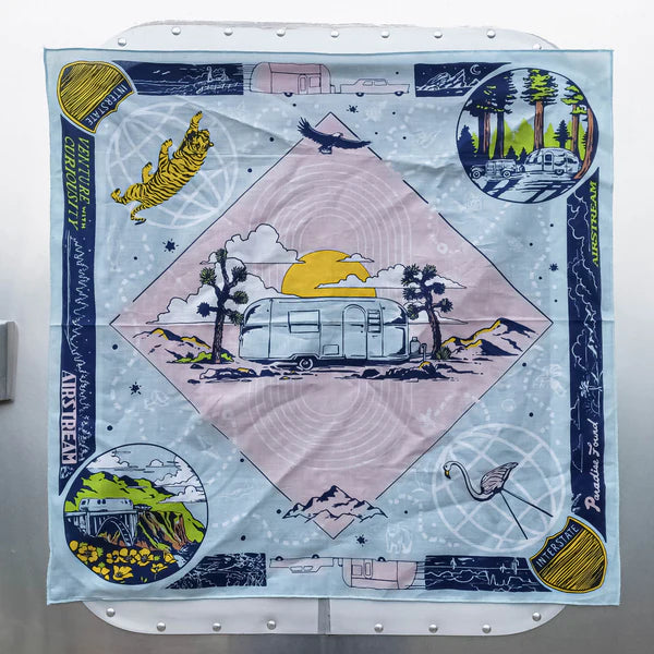 The Ace Rivington Bandits Bandana - Sky Blue Venture With Curiosity features a central illustration of an Airstream trailer with a sunset and mountain backdrop. Surrounding the image are smaller vignettes of a tiger leaping, a forest scene with a trailer, a scenic bridge, and a flamingo, along with the words 'Venture With Curiosity' and 'Airstream'.