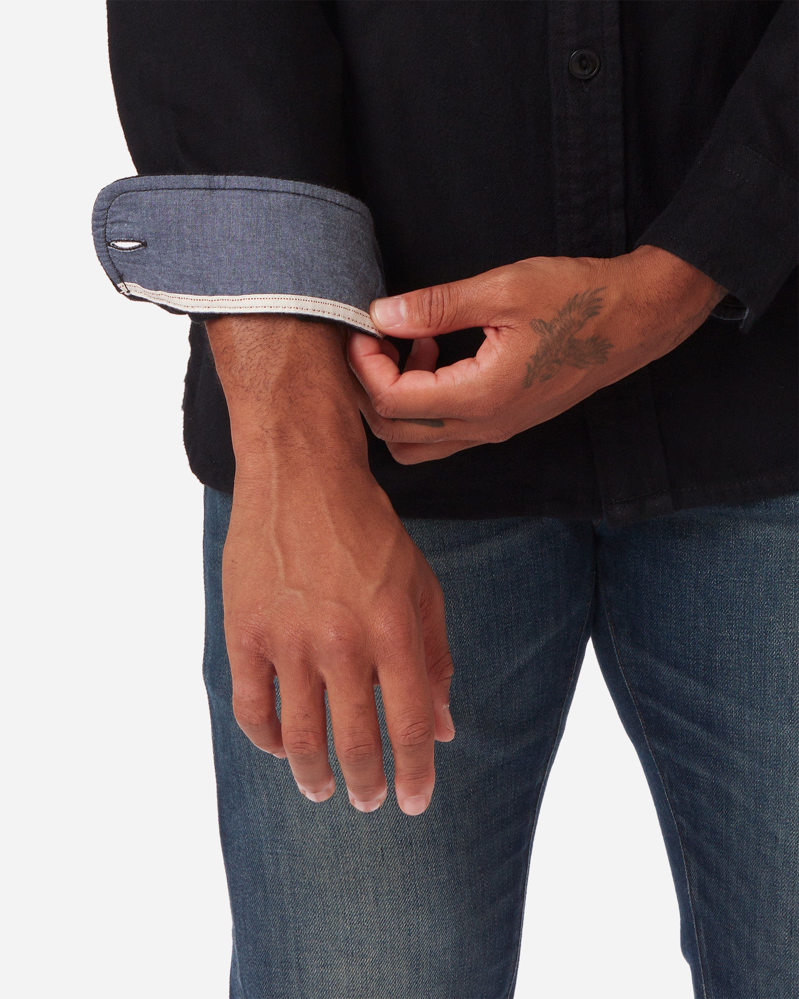 Interior right sleeve and left hand of model wearing Ace Rivington men's black soft brushed flannel shirt with color matched buttons and breast pockets and dirty vintage blue denim jeans with slight stylistic thigh wear