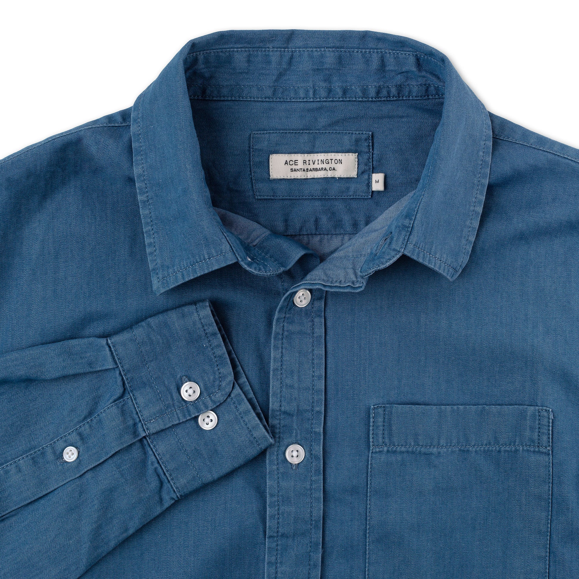 close up of cuff, collar, buttons, pocket, and tag on front of men's long sleeve tailored denim shirt in a medium wash with a single pocket and white buttons