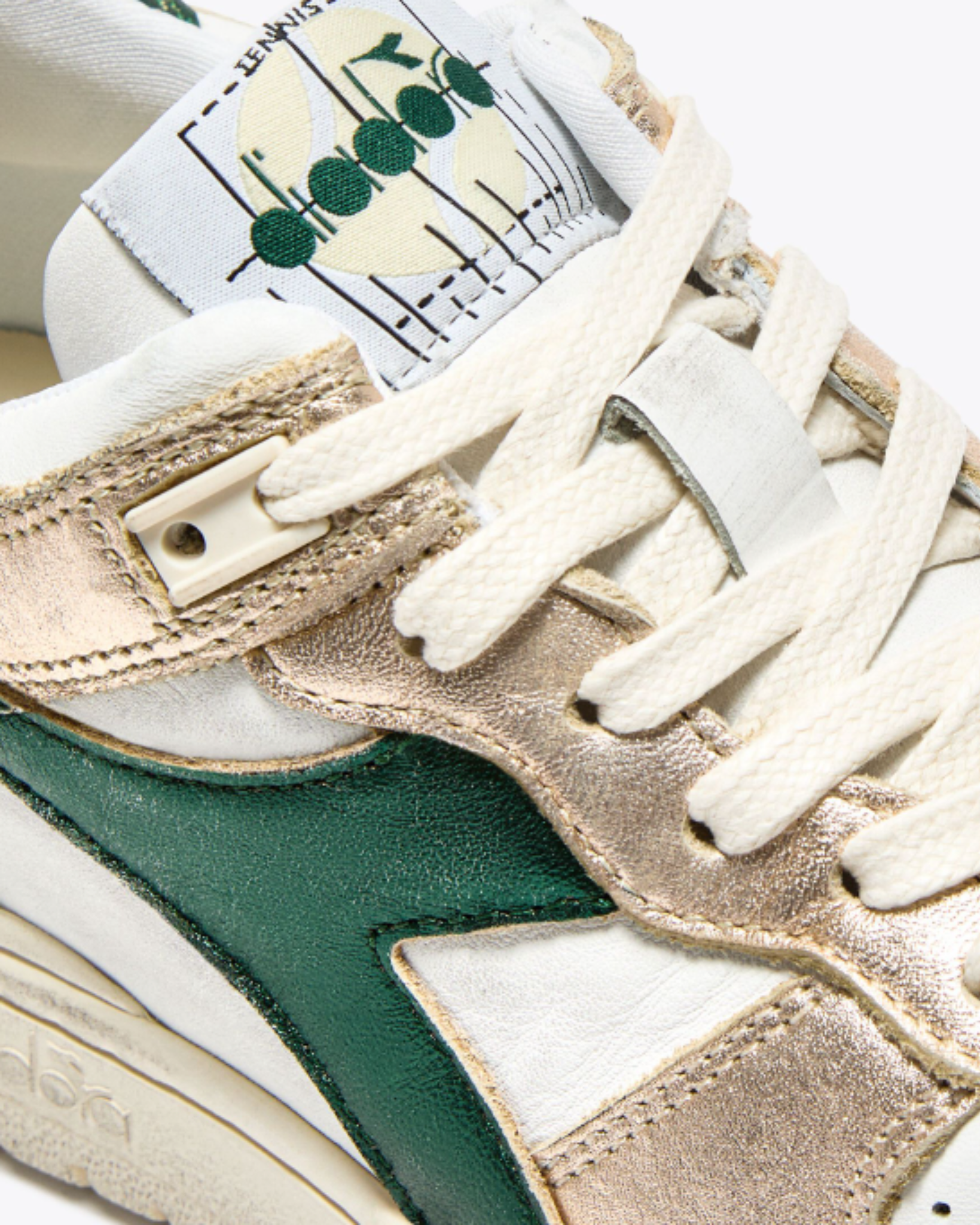 Diadora B. 560 - Metal Mix WN shoe detailed close-up of tongue branding, laces, and green side logo over metallic and white panel construction.