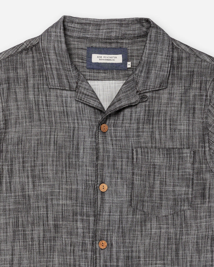 Zoomed-in collar, buttons, left-breast pocket, and interior fabric layer on flat lay of Ace Rivington "Black" Double gauze soft-textured cotton fabric camp collar shirt with coconut buttons and left-breast pocket
