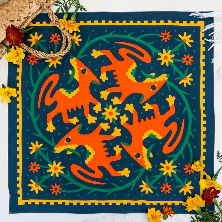 The vibrant Endless Bloom - Bandits Bandana by Ace Rivington features a dark green background decorated with colorful illustrations of foxes or dogs, yellow and orange flowers, and green vines. The bandana has a yellow geometric border, with real yellow and red flowers accentuating the lively design.