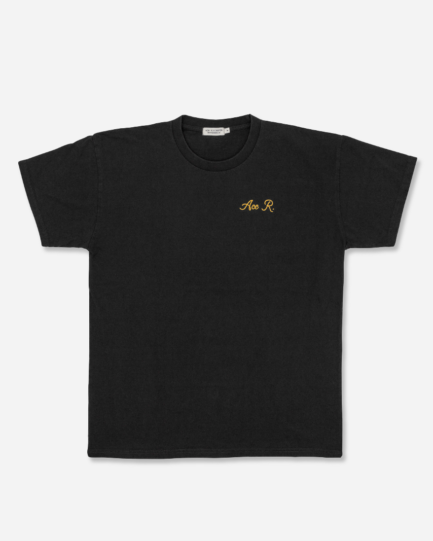 front of men's black graphic tee with gold cursive lettering reading "Ace R." over the left breast area