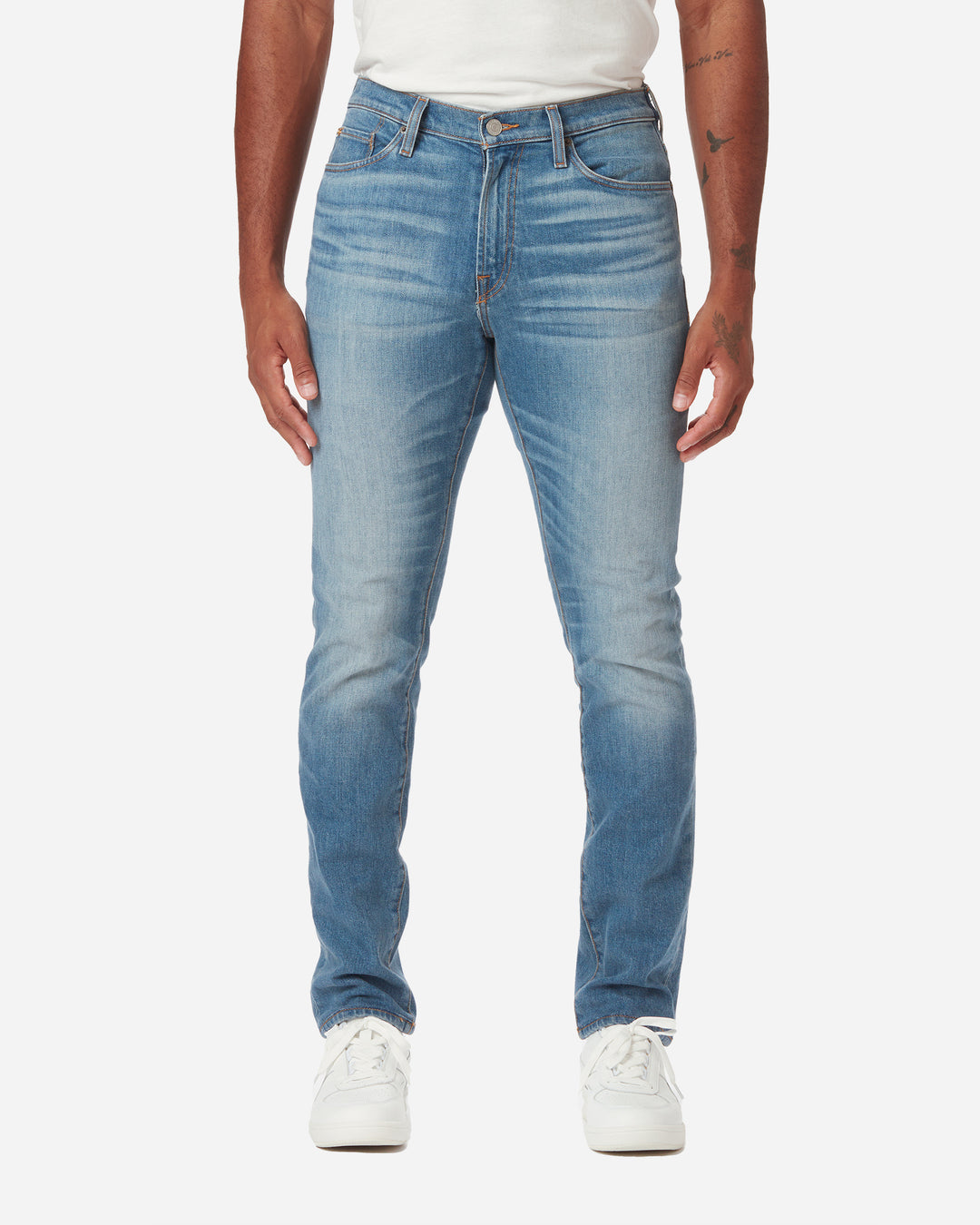 model facing directly forward wearing close up of stitching on pair of men's athletic taper medium light blue jeans with slight wear along the thigh area with a pair of white Diadora B Elite sneaker shoes and tucked white Ace Rivington super soft supima short-sleeved tee shirt