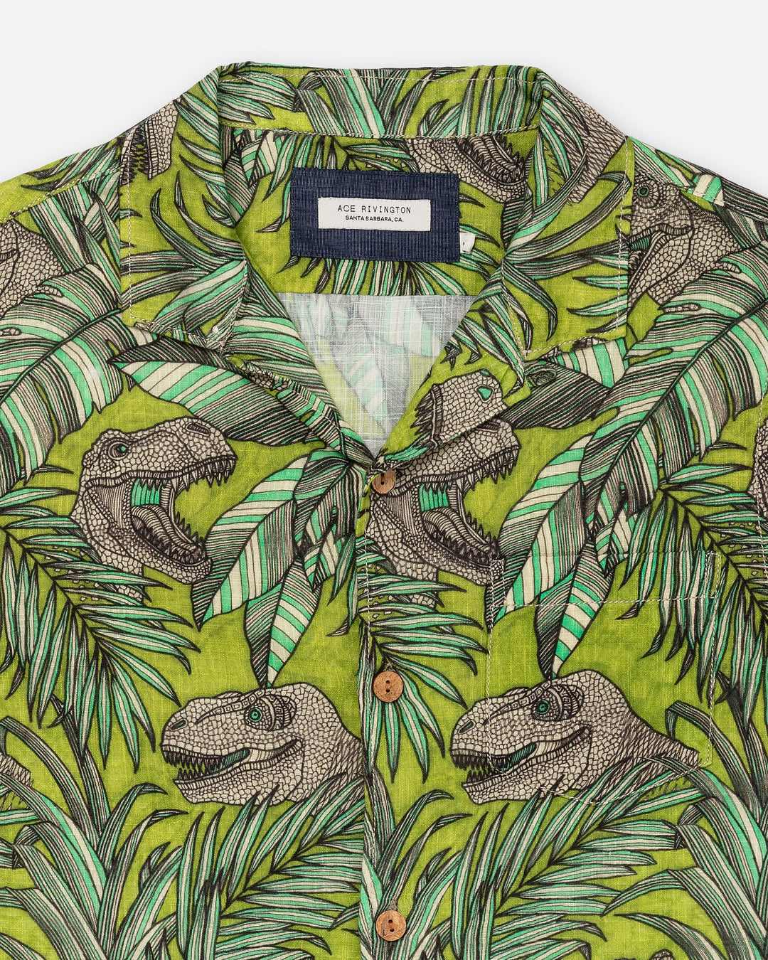 Zoomed-in detail shot of flat lay of front of Ace Rivington "Man Eater" green and brown floral-themed camp shirt with leaf and dinosaur design with left breast-pocket and emphasized inner layer of doubles-gauze textured fabric and brown wooden buttons