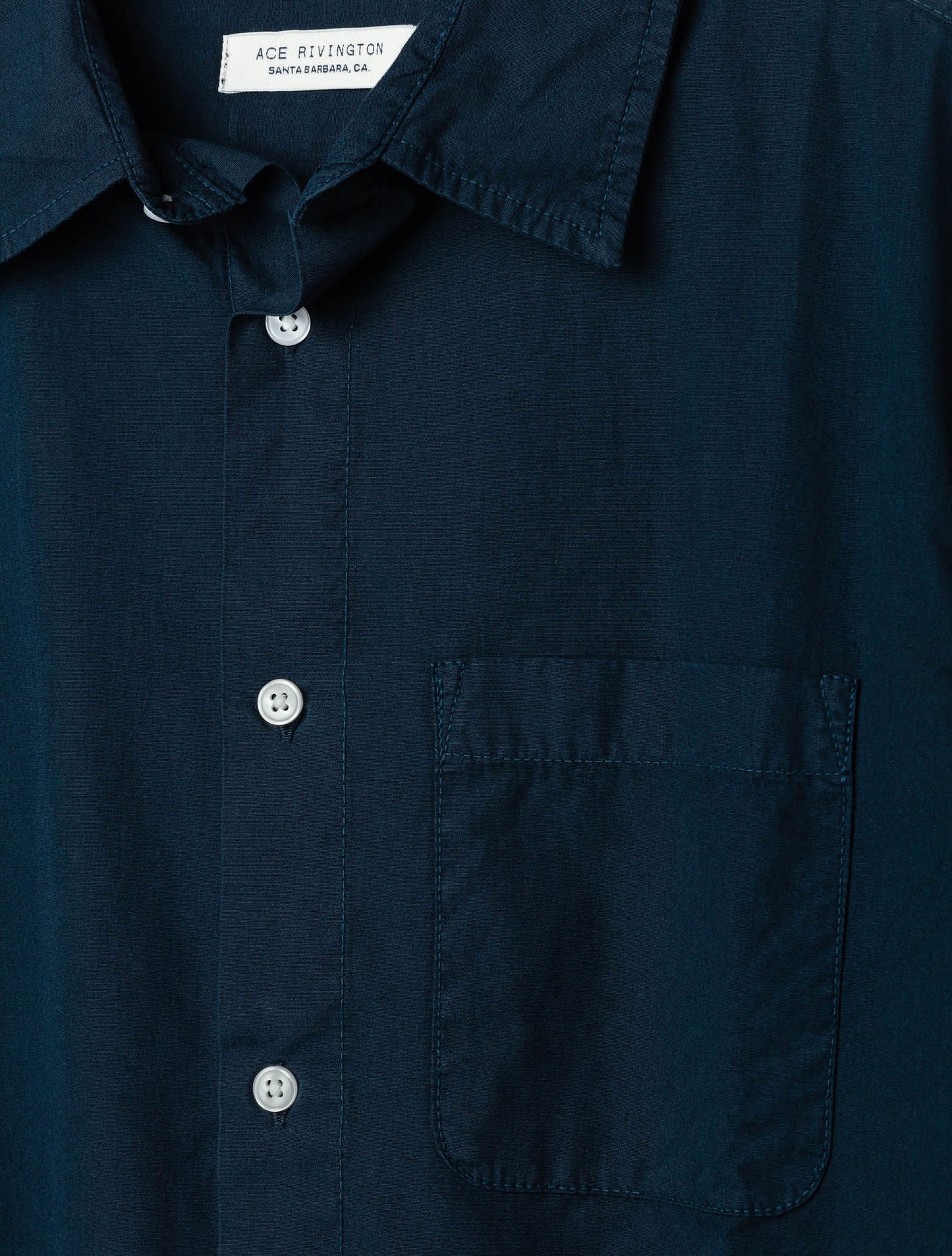 close up of collar, buttons, pocket, and tag on front of men's navy long sleeve tailored poplin shirt with pearl buttons and a single pocket in shorter-hem height option
