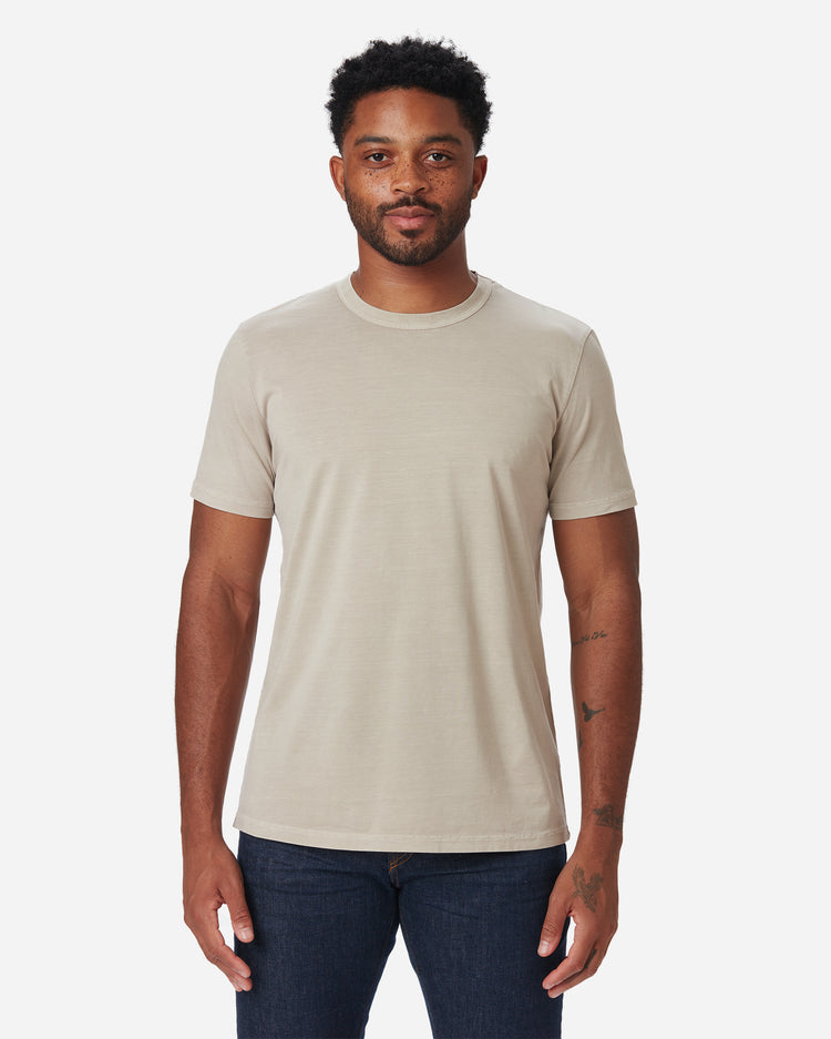 model facing directly forward wearing Ace Rivington long staple light beige sand coloredsuper soft short-sleeved cotton shirt and dark clean deep indigo colored pair of Ace Rivington denim jeans