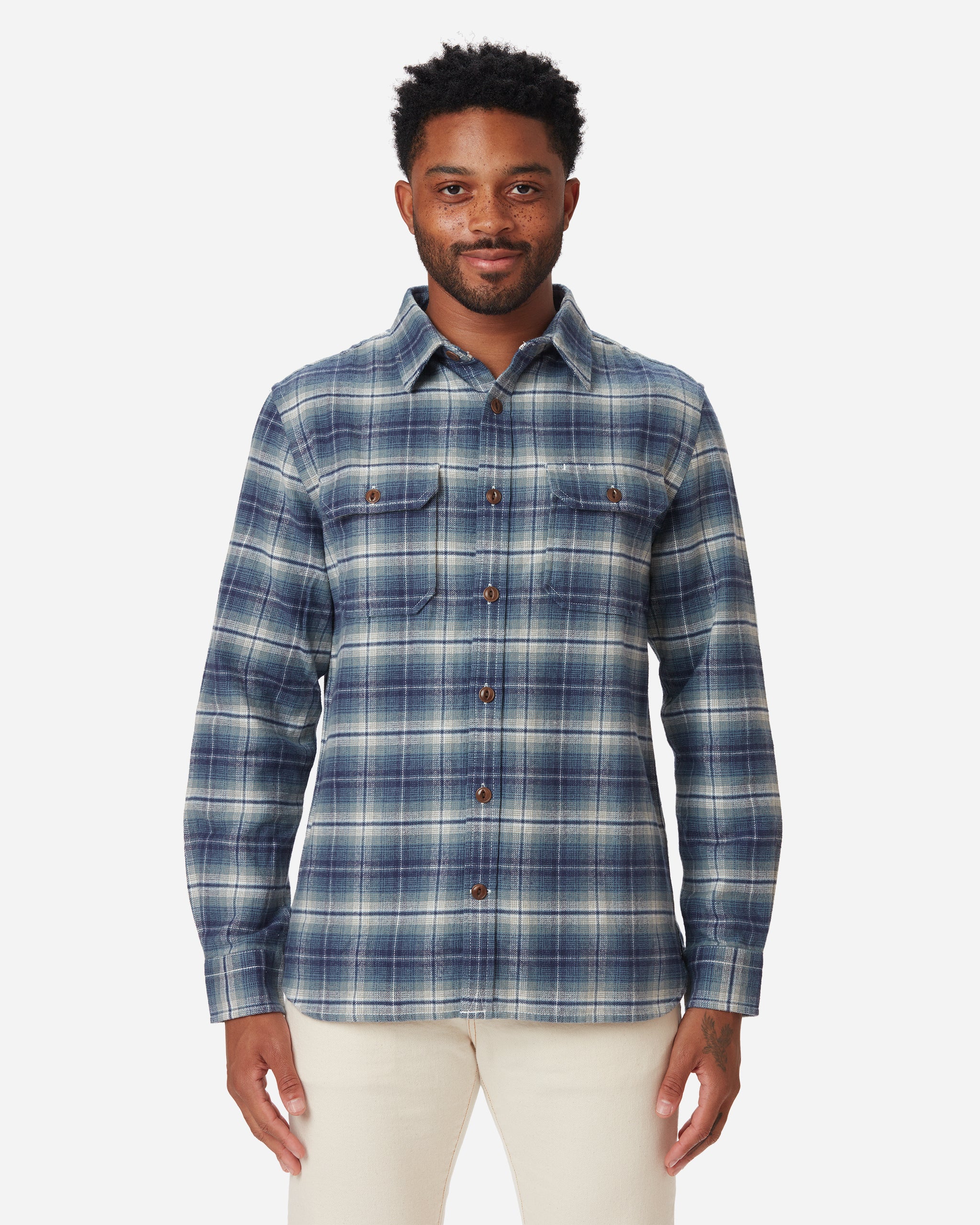 Model facing directly forward wearing men's off white and light blue plaid pattern flannel with brown buttons and white collar stripe and Ace Rivington Ecru colored denim jeans