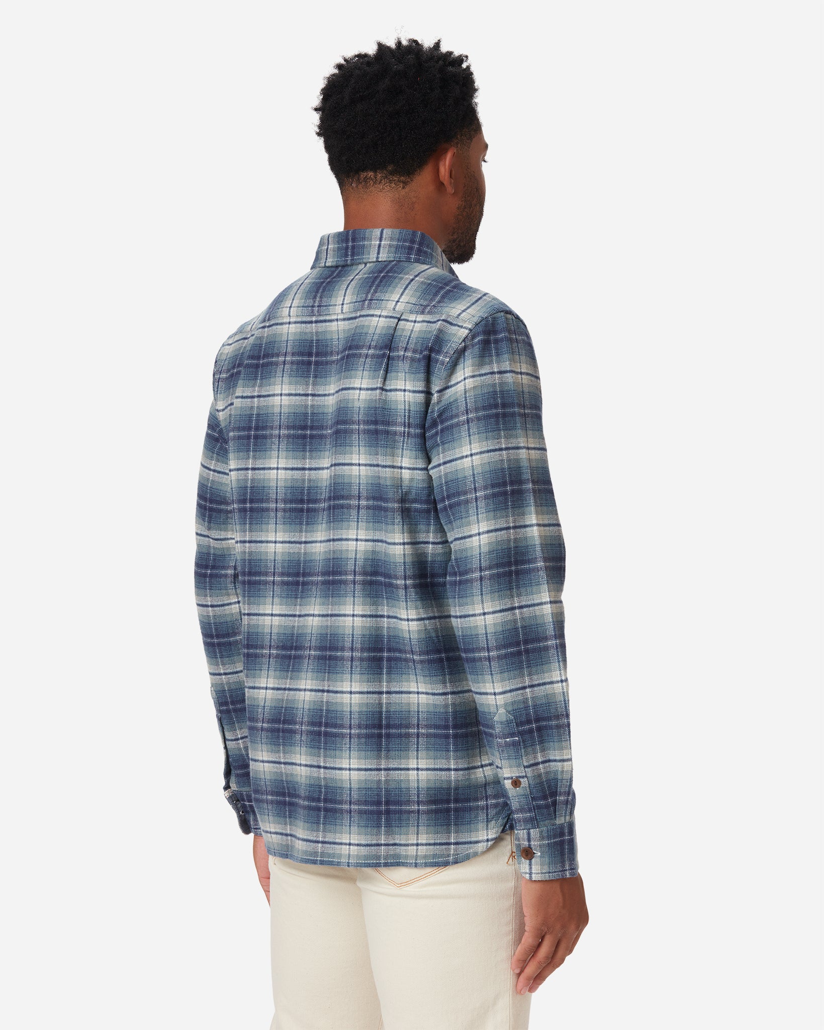 back of model with rightward gaze wearing men's off white and light blue plaid pattern flannel with brown buttons 