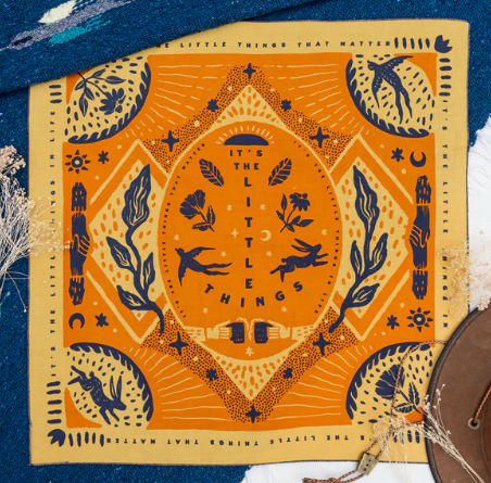 The vibrant The Little Things - Bandits Bandana by Ace Rivington features an orange background with blue and white illustrations of birds, leaves, and stars, framed by a border with the phrase 'The Little Things That Matter.'