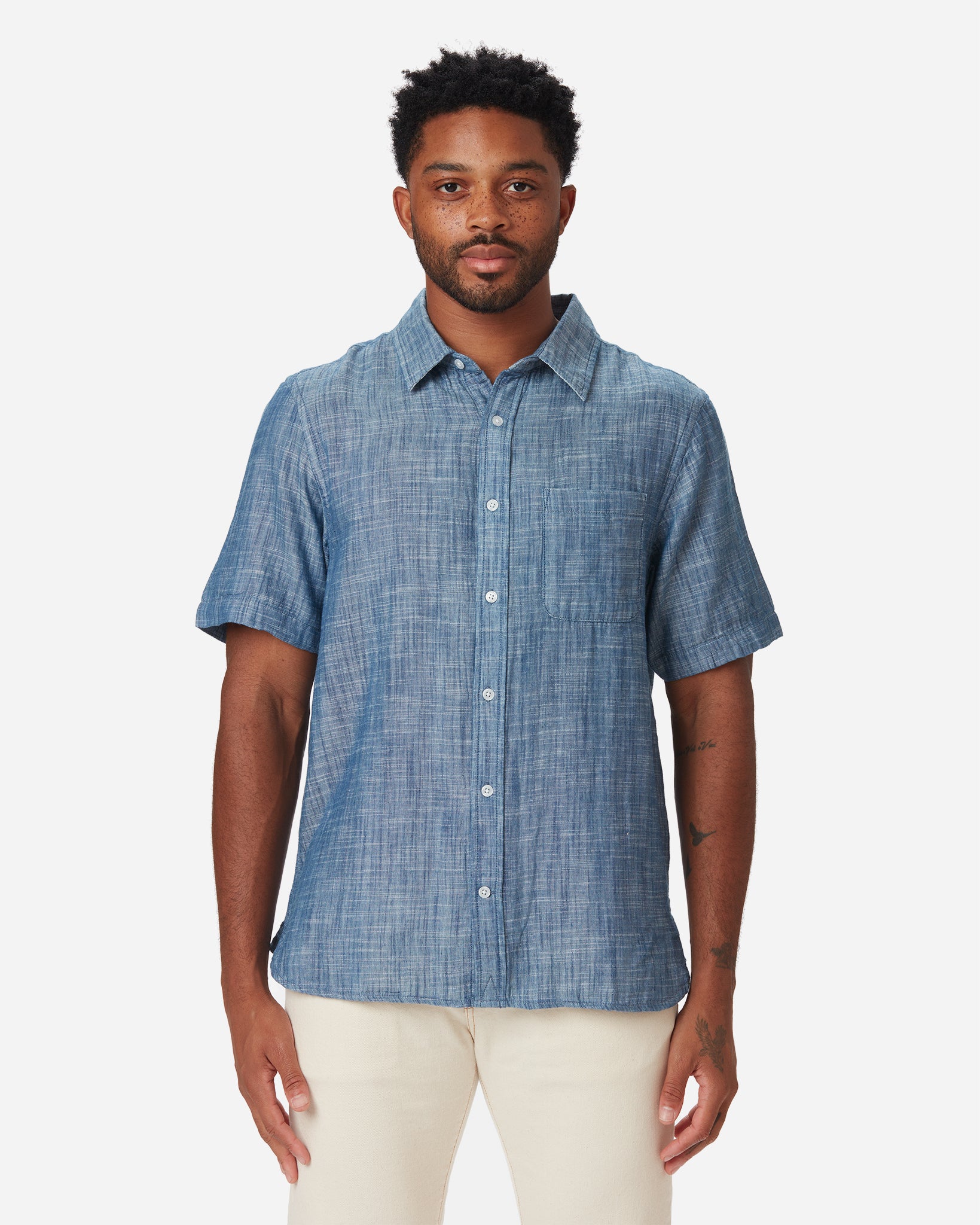 Model with a directly frontward gaze wearing Ace Rivington short-sleeved indigo slub soft textured-cotton shirt with linen hand feel, pearl buttons, left-breast pocket, collar, and off white interior and a pair of Ace Rivington ecru color denim jeans