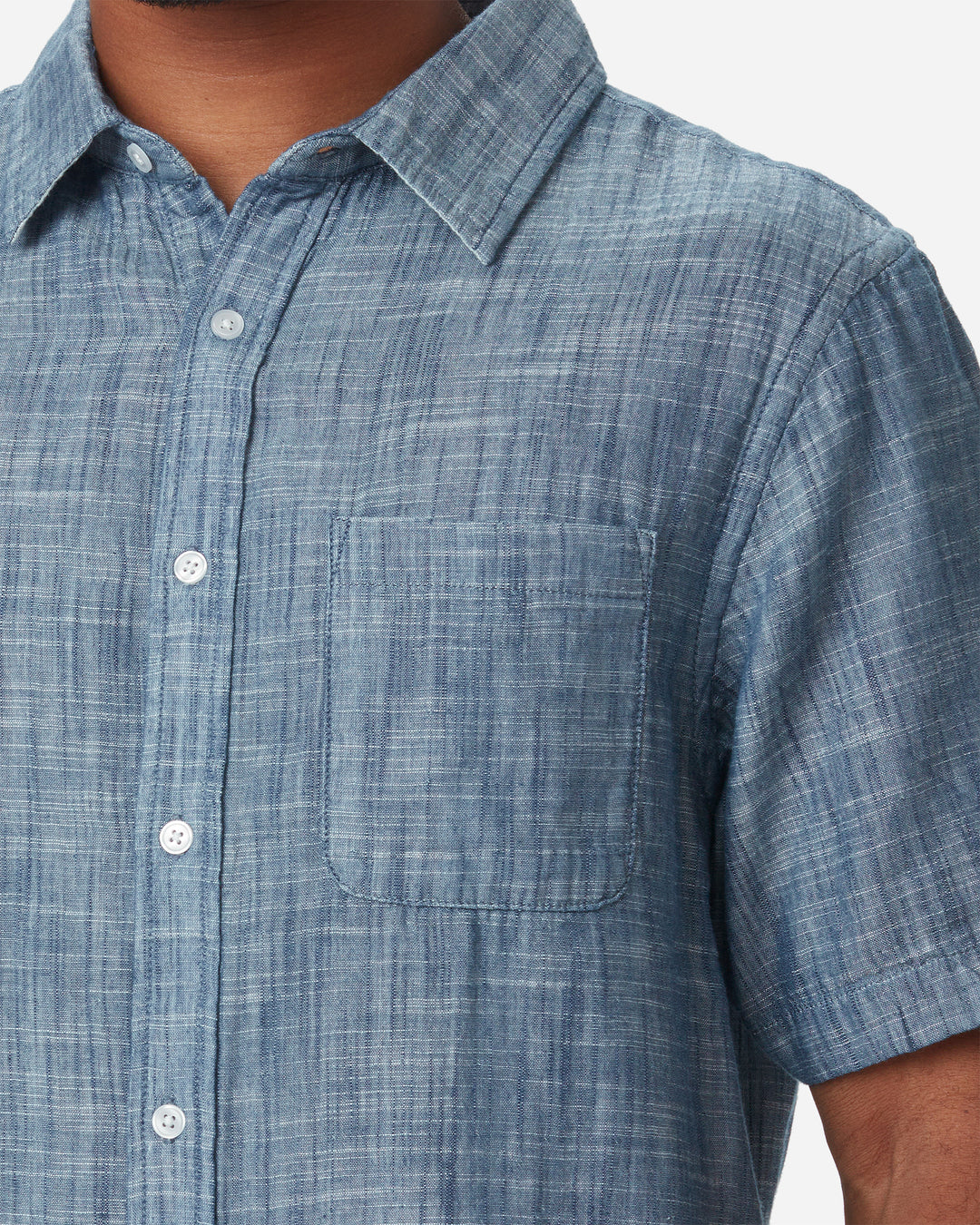 Zoom in of neck, pocket, buttons, and collar of model wearing Ace Rivington short-sleeved indigo slub soft textured-cotton shirt with linen hand feel, pearl buttons, left-breast pocket, collar, and off white interior