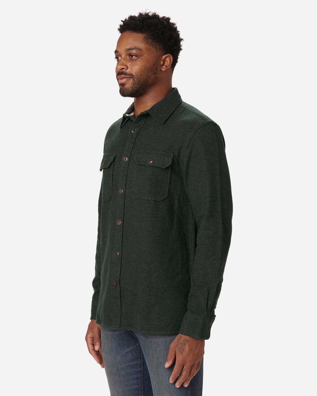 Side of rightward facing model wearing Ace Rivington men's forest green flannel with brown buttons and a white collar stripe