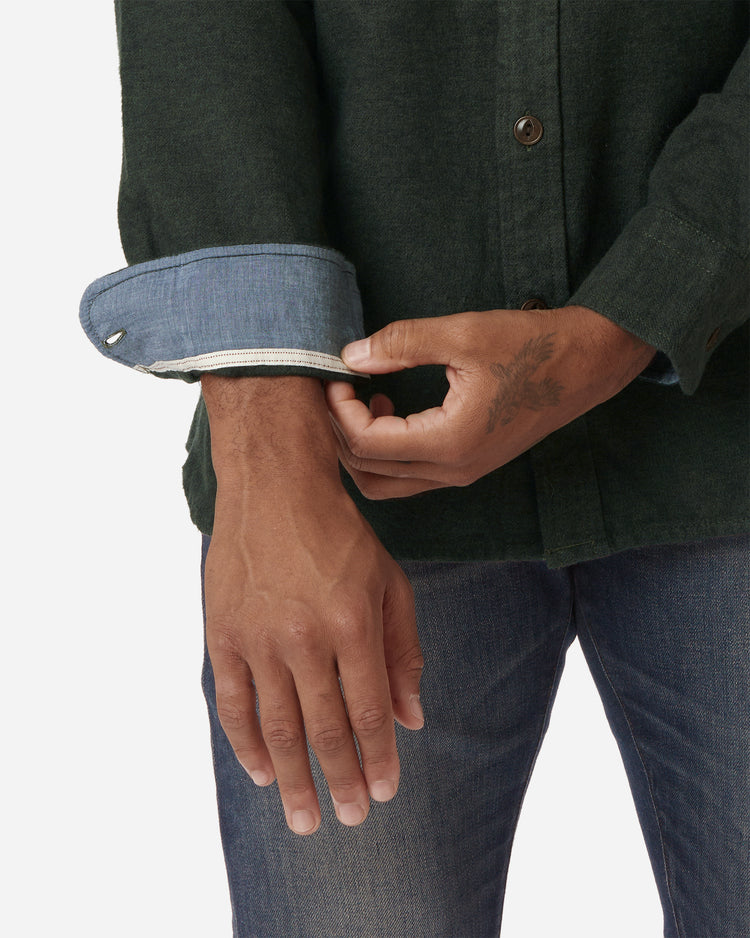 interior right sleeve and left hand of model wearing Ace Rivington men's forest green flannel with brown buttons and a white collar stripe and Ace Rivington dirty vintage blue denim jeans