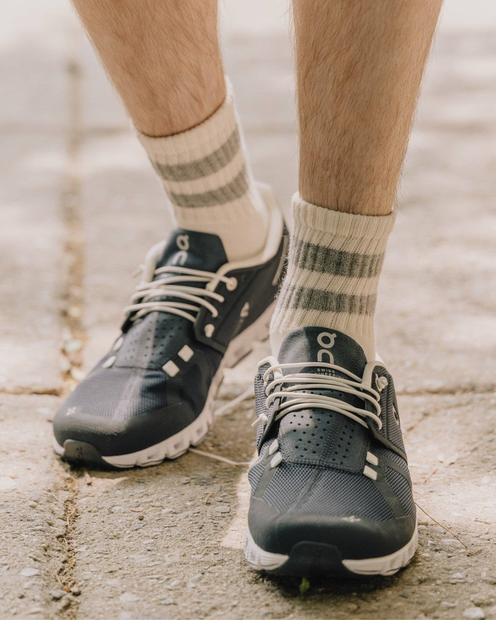 The Mono Stripe Quarter Crew – Grey: Street-level view of The Mono Stripe Quarter Crew with grey stripes styled with black On Running shoes on pavement.