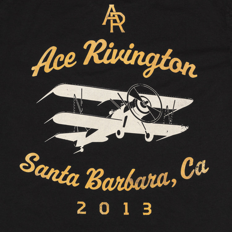 close up of back of men's black graphic tee with yellow logo print reading "AR" positioned diagonally in center back above a white biplane graphic which is above yellow text reading "Santa Barbara, Ca 2013"