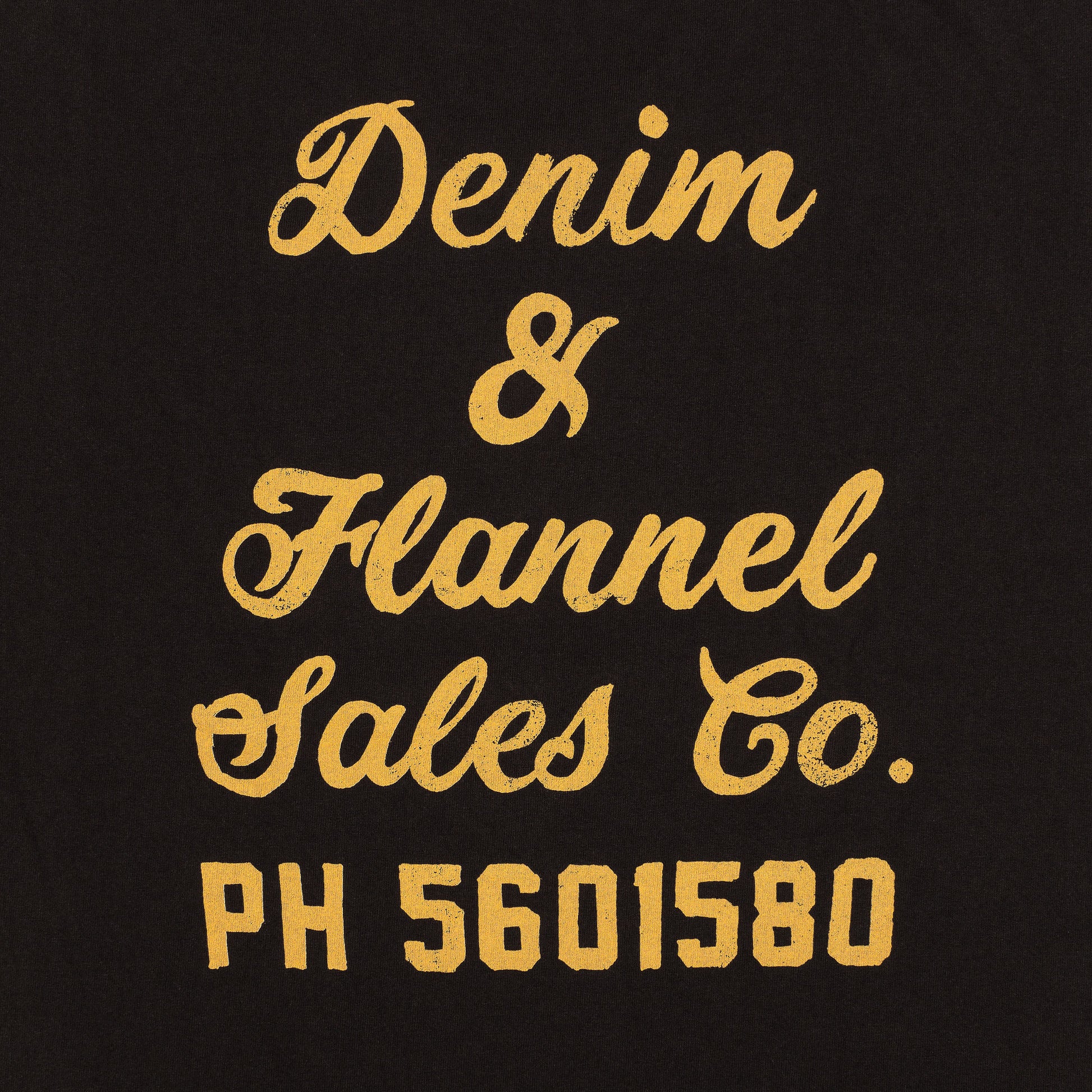 close up of back of men's black graphic tee with yellow print reading "Denim & Flannel Sales Co." in cursive above yellow block letteting reading "PH 5601580"