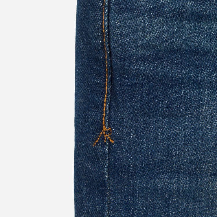 close up of stitching on pair of men's athletic taper blue jeans with slight wear 