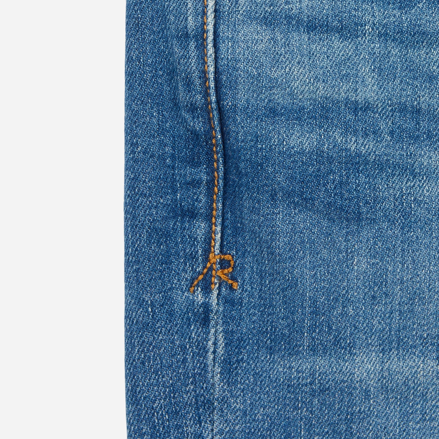 close up of stitching on pair of men's athletic taper medium light blue jeans with slight wear 