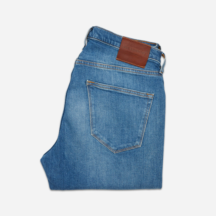 back of folded pair of men's athletic taper medium light blue jeans with slight wear 