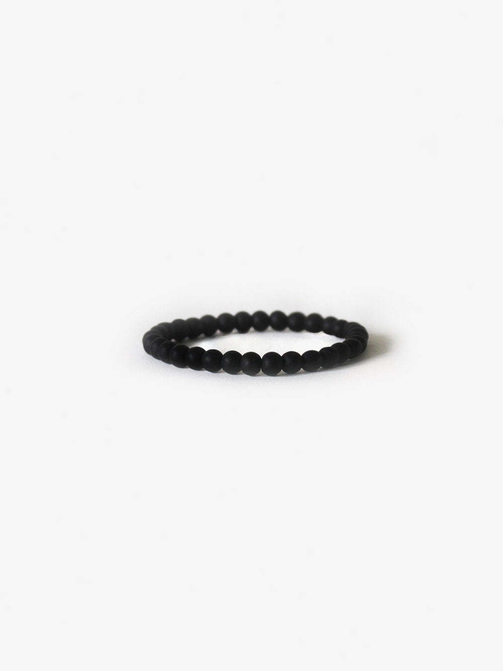 The Ace Rivington Branco - Earth Bracelet in Matte Black Onyx features a simple yet elegant design. The bracelet is composed of uniformly sized, matte black onyx beads strung together to form a continuous loop. The matte finish of the beads gives the bracelet a sleek and understated appearance, making it a versatile accessory suitable for various outfits and occasions.