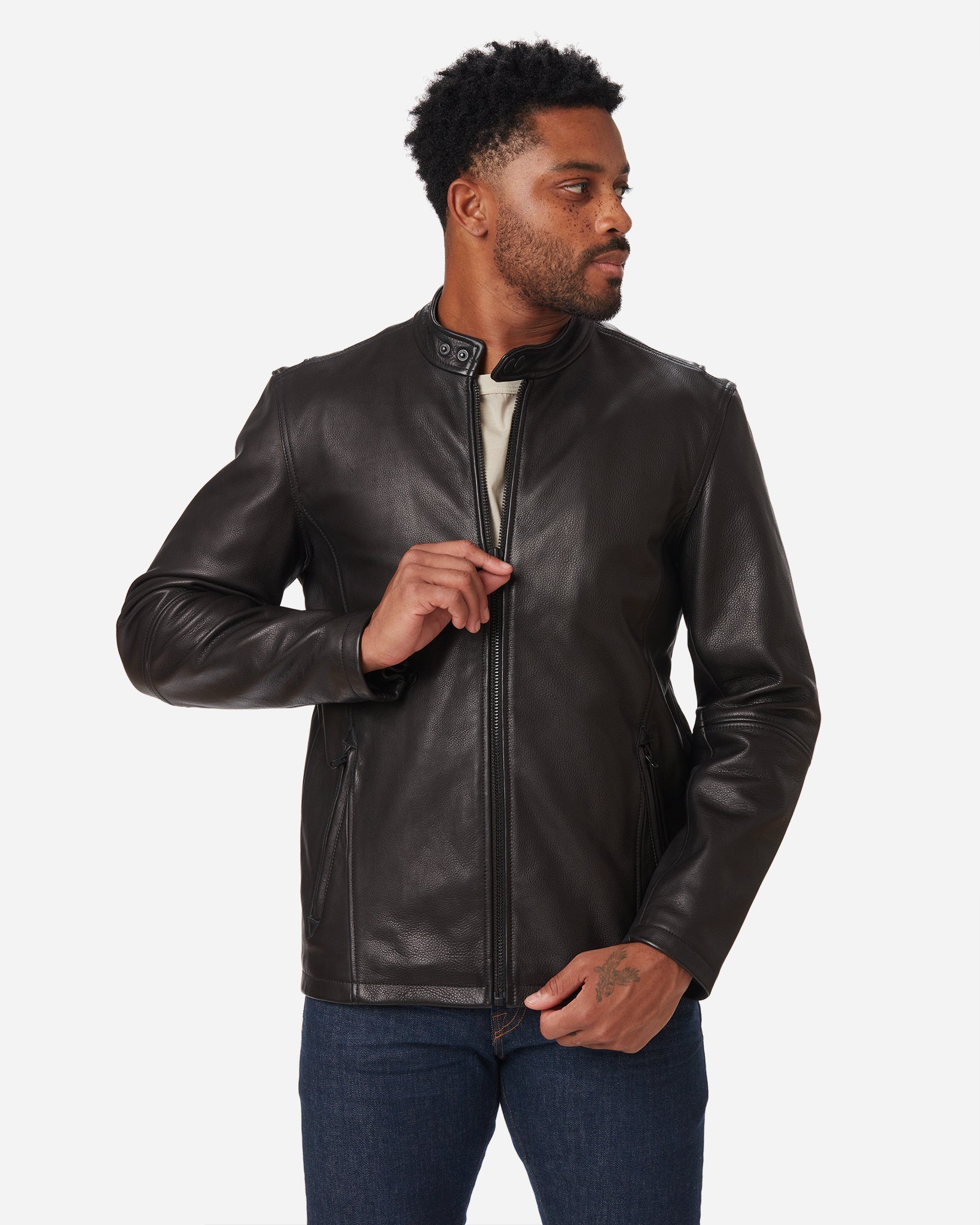 Man wearing Ace Rivington Cowhide - Cafe Racer - Vintage Black Jacket with a front zipper and a stand-up collar and blue jeans pair with a white shirt underneath the jacket. The jacket appears to be made of Super Soft Leather material. 