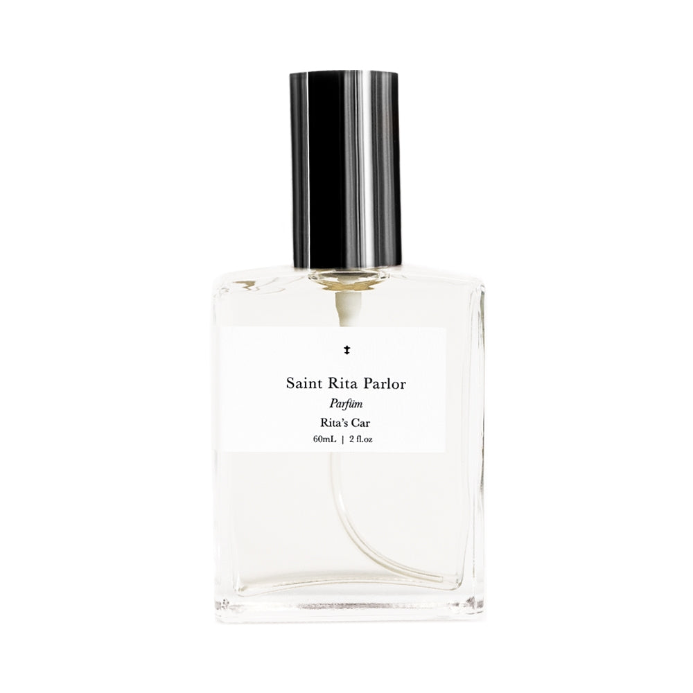 A clear glass bottle of Ace Rivington Saint Rita Parlor Rita’s Car parfum with a volume of 60 ml (2 fl oz). The bottle features a sleek black cap and a minimalist white label that reads 'Saint Rita Parlor Parfum Rita’s Car.'