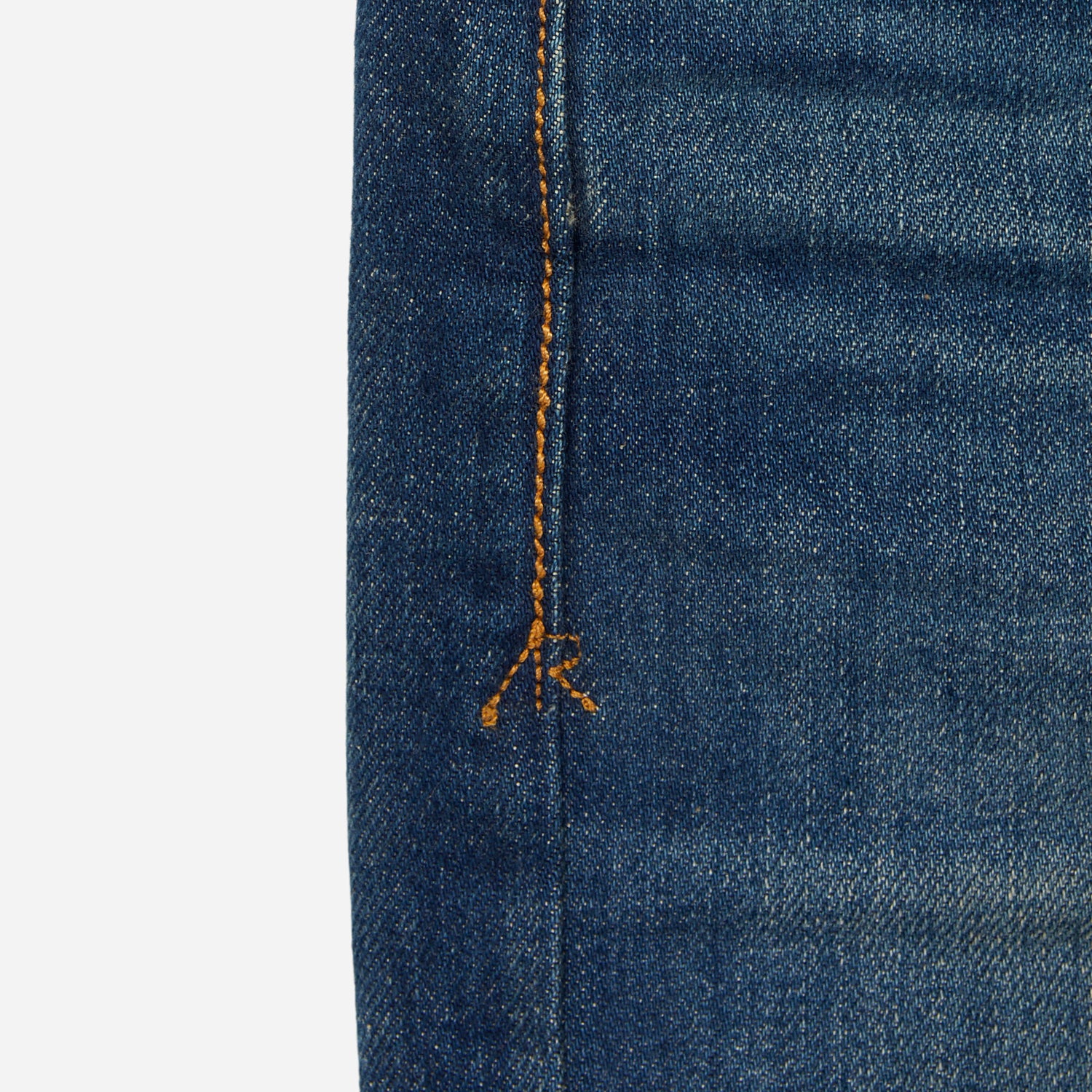 close up of stitching of pair of high quality slim cut men's green hue blue jeans with slight wear
