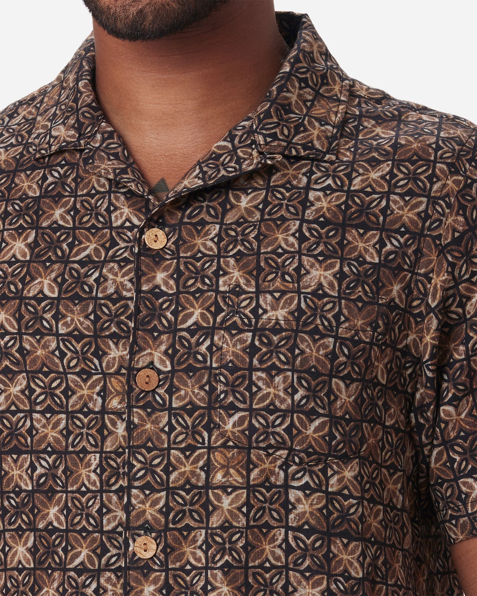 Zoomed-in neck, left-breast pocket, buttons, and collar on model wearing  Ace Rivington "Vintage Tile" gold, brown, and black exclusive design camp-collar shirt with coconut buttons and doubles-gauze soft-textured cotton fabric 